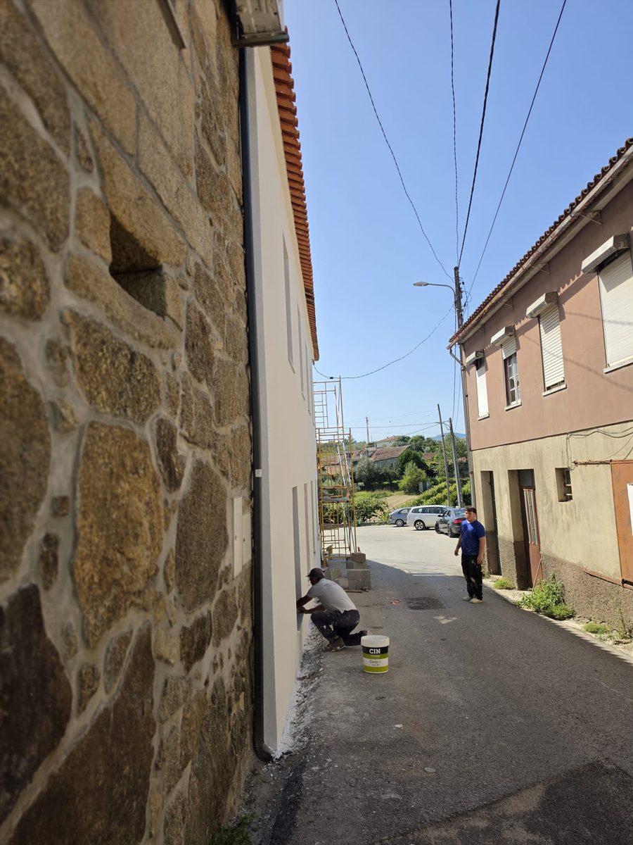 Fachada acabada e pintada de branco, junto a uma parede de pedra